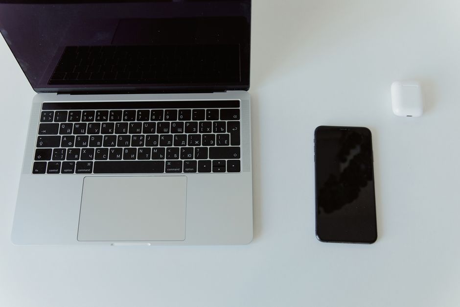 Modern minimalist workspace featuring a laptop, smartphone, and wireless earbud case on a white table.