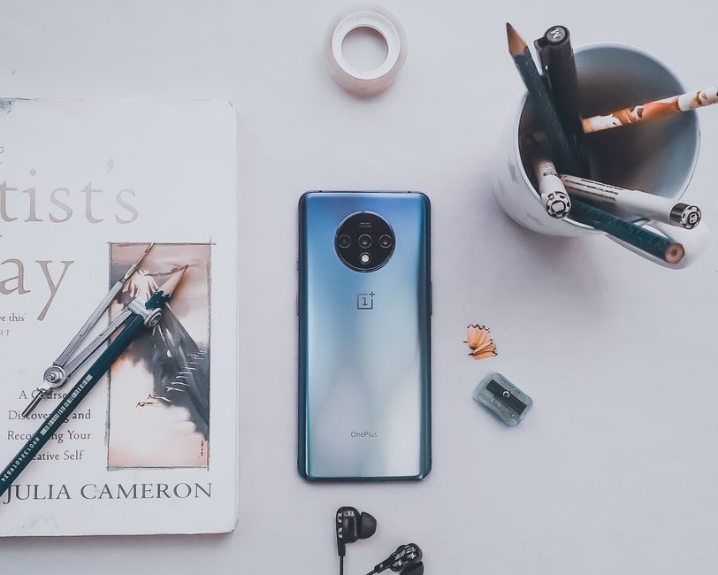 Top view of contemporary cellphone near glass with pencils and book on white table