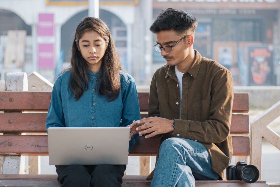 Two young adults collaborating on a laptop outdoors, showcasing teamwork and digital learning.