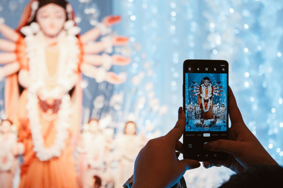 Hands holding a smartphone capturing a Hindu goddess statue, blurred background.