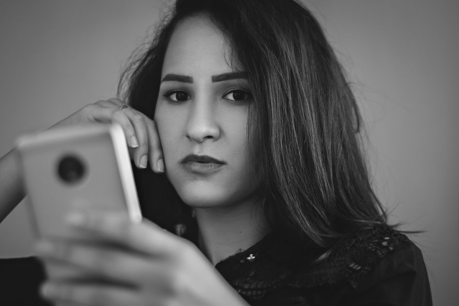 A black and white portrait of a young woman using a smartphone indoors.