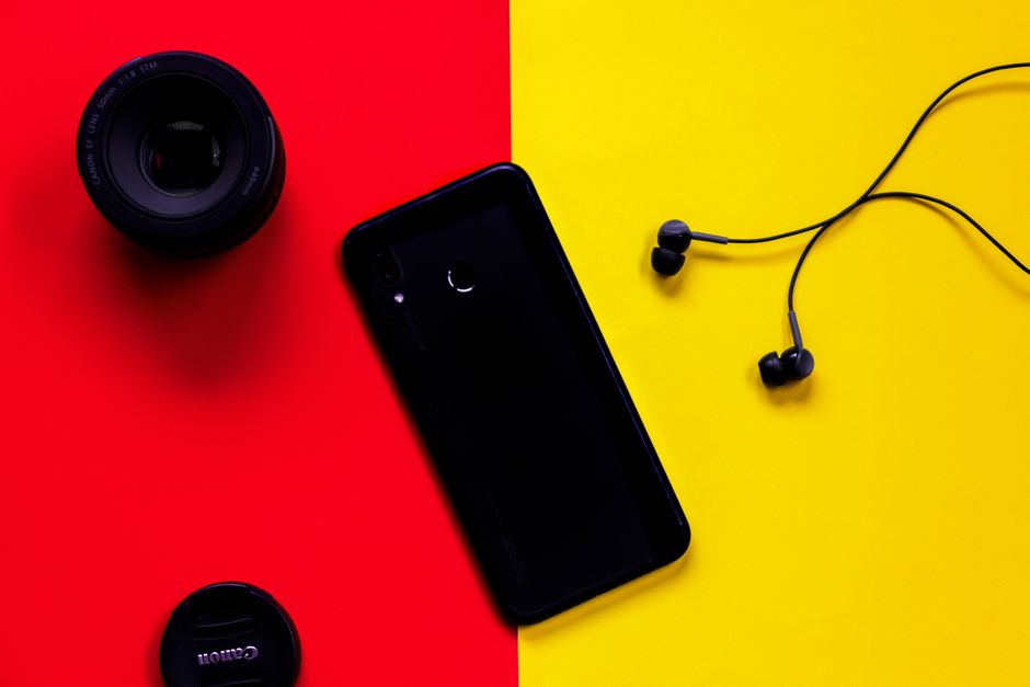 Colorful flat lay featuring a smartphone, camera lens, and earphones on a red and yellow background.