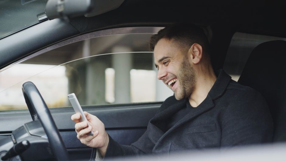 Young man enjoying a moment with his smartphone inside a car.