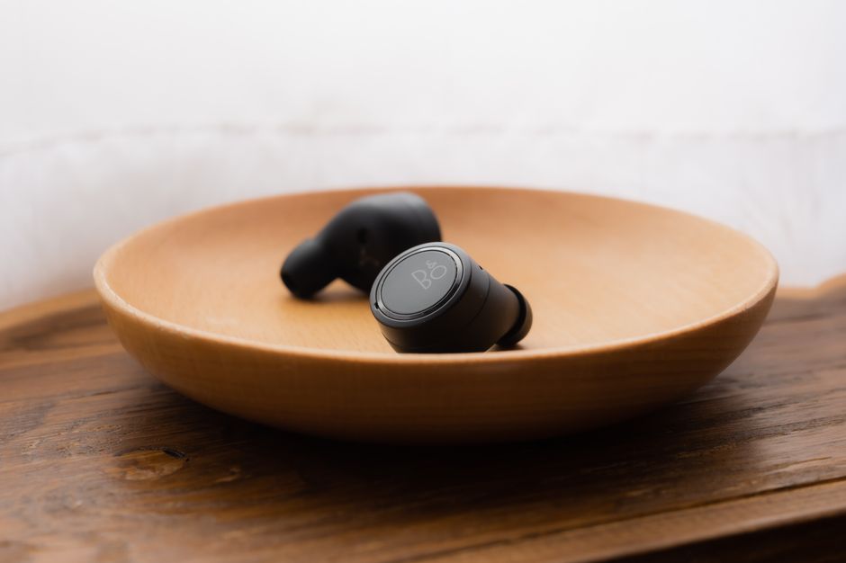 Close-up of black wireless earbuds placed in a stylish wooden bowl on a wooden surface.