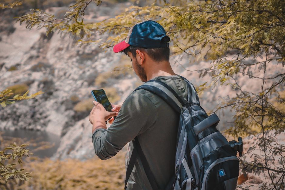 A young man hiking outdoors, using a smartphone in the scenic landscape of New Delhi, India.