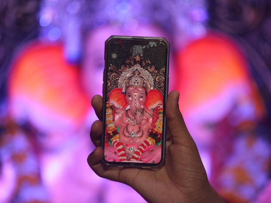 Hand holding a smartphone displaying Lord Ganesha amidst colorful festival lights.