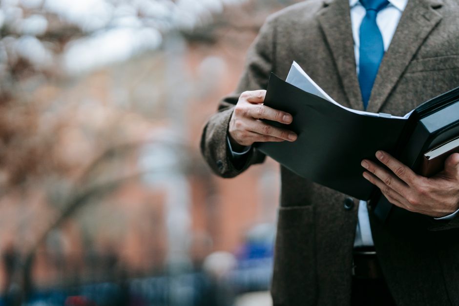A professional in formal wear reviewing documents outside, showcasing business attire and focus.